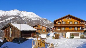 A wooden chalet with a balcony, a ski lift, and a mountain backdrop.