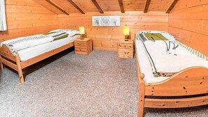 A wooden cabin bedroom with two single beds, a small nightstand with a lamp, and a framed picture on the wall.