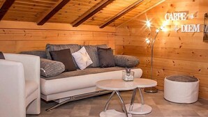 A cozy log cabin interior with a sofa, two armchairs, a small round table, and a floor lamp.