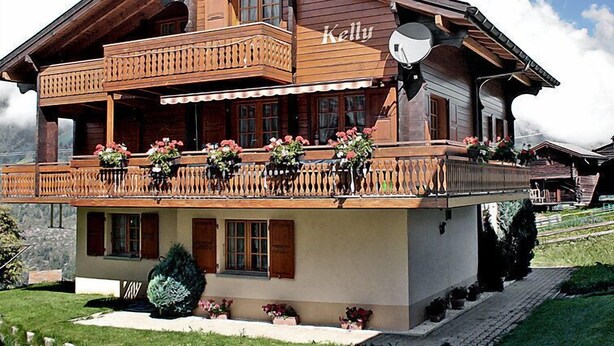 A wooden chalet with a balcony, a satellite dish, and a name 'Kelly' on the side.