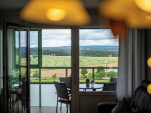 Ein Zimmer mit großem Fenster und Blick auf eine grüne Landschaft mit Feldern und Bäumen.