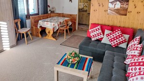 Kodikas olohuone, jossa on sohva, ruokapöytä tuoleineen, sohvapöytä ja taustalla keittiötila.