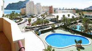 Hotel com piscina, palmeiras e vista para o oceano e montanhas.