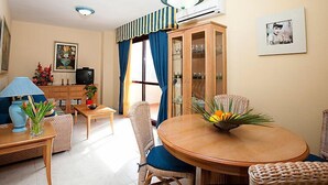 Uma sala de estar bem iluminada, com área de jantar, televisão e um armário com portas de vidro.