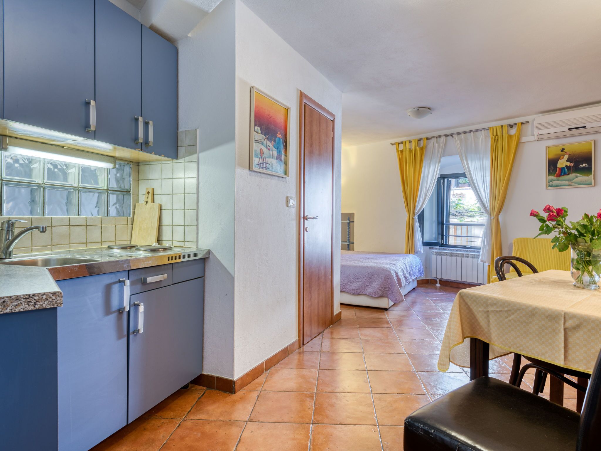 A compact kitchen with blue cabinets, a tiled backsplash, and a window with a view.