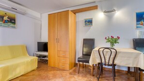 Una habitación con un sofá amarillo, una mesa de comedor con sillas, un armario de madera, un televisor y un cuadro en la pared.