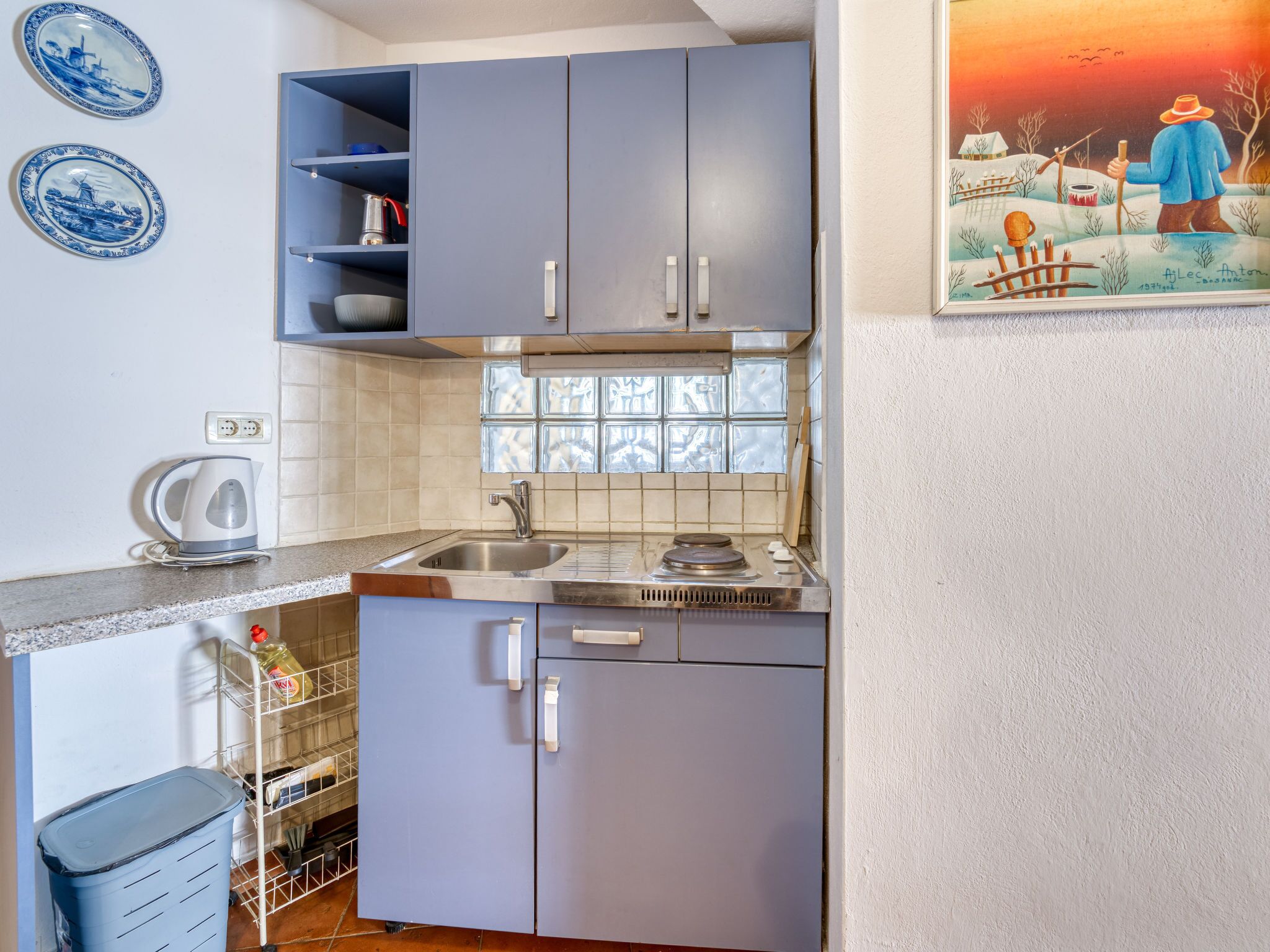 Een kleine keuken met grijze kastjes, een roestvrijstalen spoelbak en een betegelde achterwand.