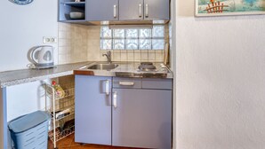 Una cocina compacta con gabinetes grises, un lavamanos de acero inoxidable y un salpicadero de azulejos.
