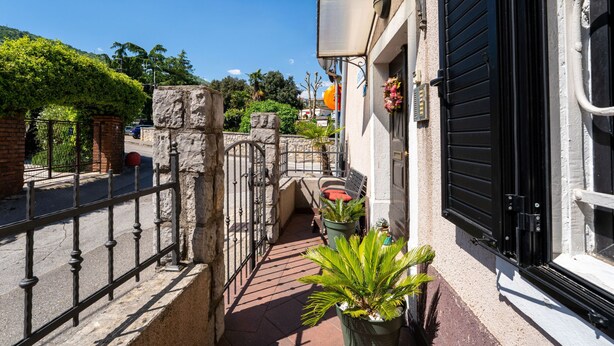 Un callejón estrecho con una reja de metal, plantas en macetas y un edificio con una puerta persiana negra.