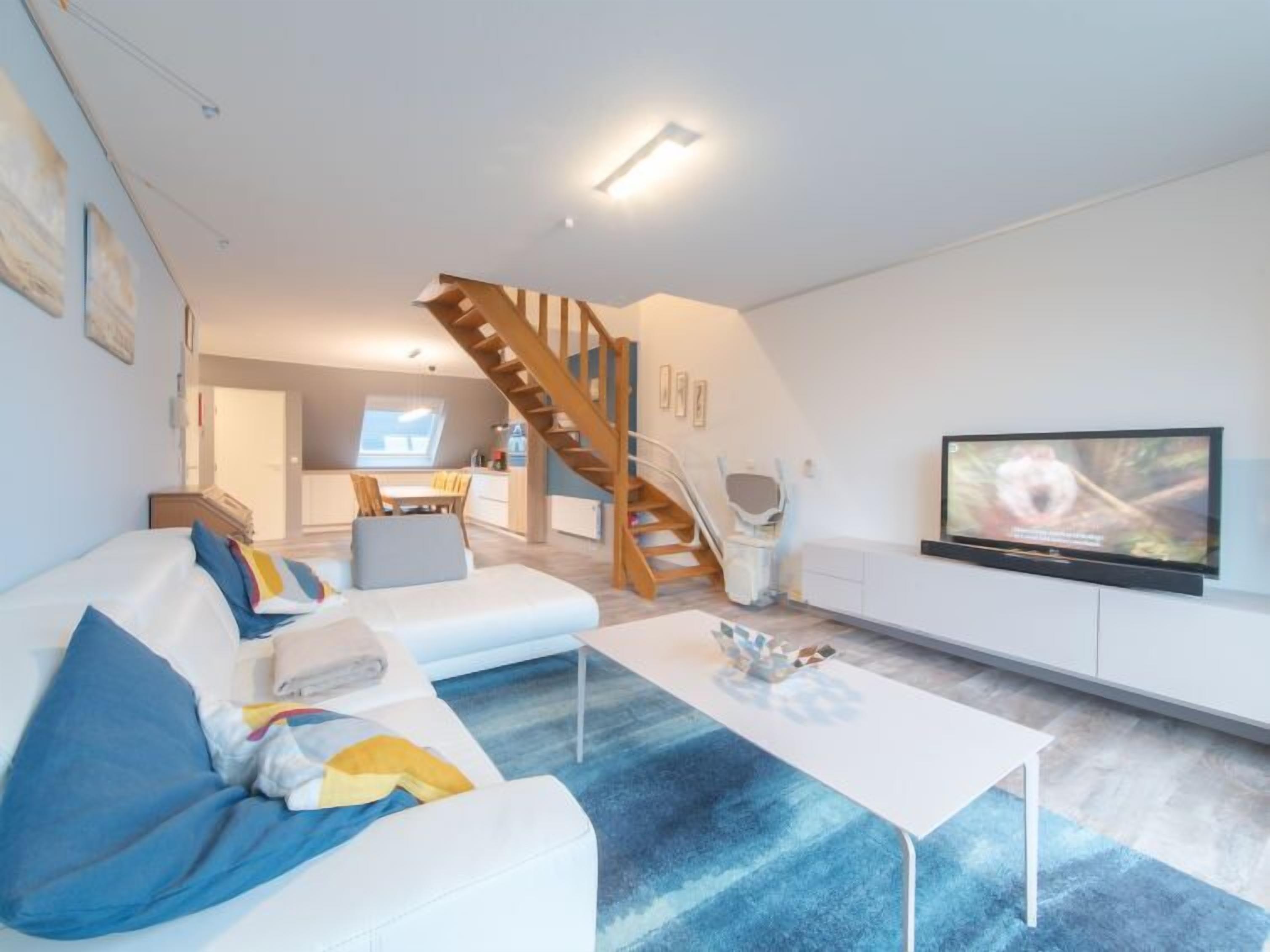 Een moderne woonkamer met een bank, salontafel, televisie en een trap naar een hoger niveau.