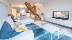 En moderne stue med sofa, sofabord, fjernsyn og en trappe til et øvre plan.