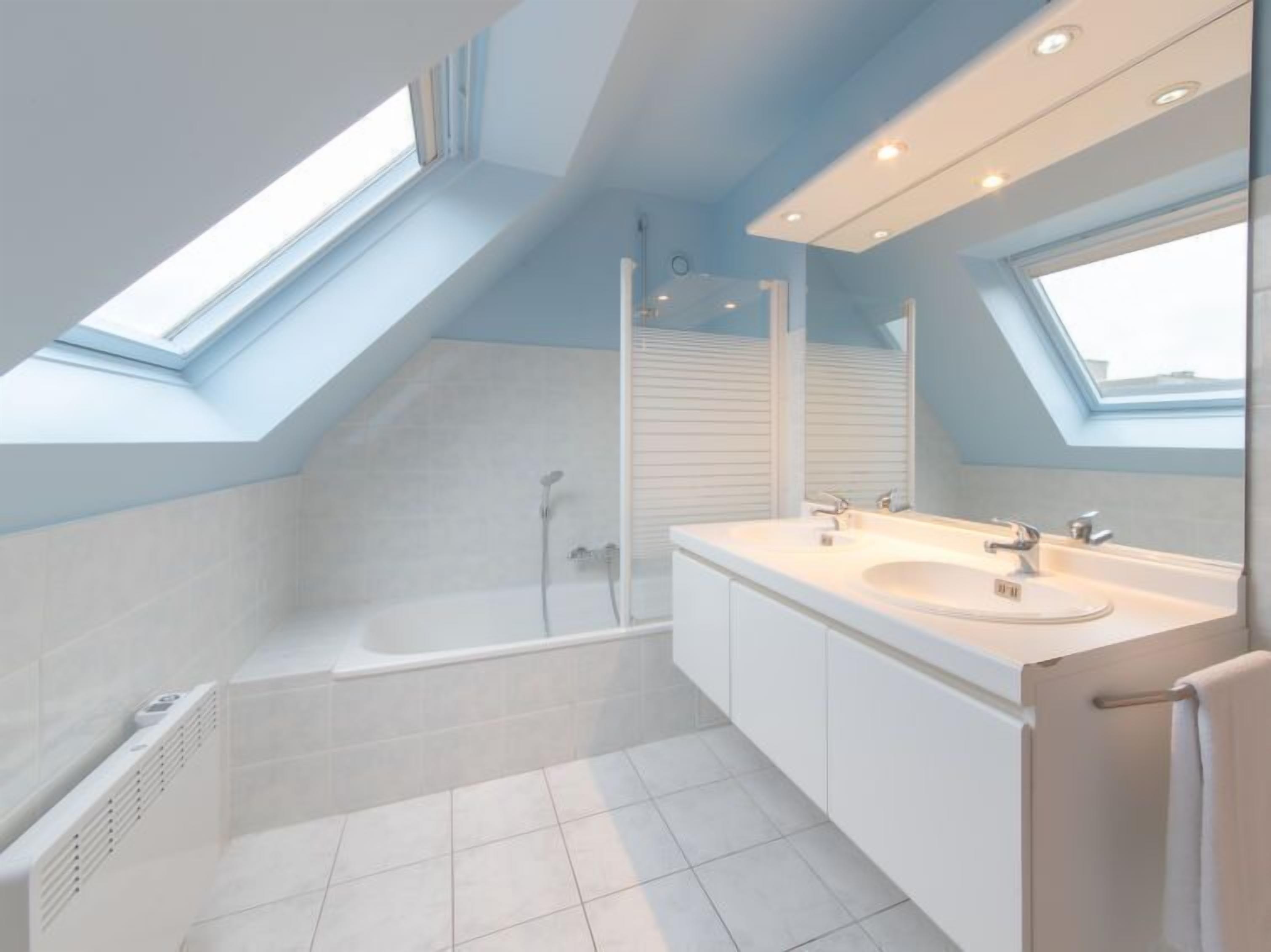 A modern bathroom with a skylight, a bathtub, a shower, and a vanity with a mirror.