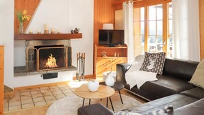 Una sala de estar acogedora con chimenea, un sofá de cuero, televisión y vistas al exterior.