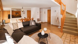 Una sala de estar moderna con un sofá de cuero negro, una mesa redonda y una escalera con barandillas de madera.