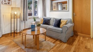 Een gezellige woonkamer met een gestreepte bank, een ronde houten tafel en een grote spiegel boven de deur.