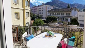 Ein Balkon mit Tisch und Stühlen, Blick auf einen Berg und Gebäude im Hintergrund.