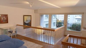 Ein geräumiger Raum mit großem Fenster, einer Holztreppe und einem Bett mit blauer Bettwäsche.