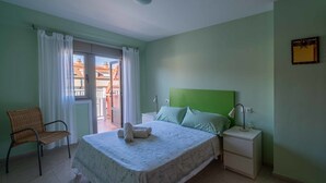 Un dormitorio con cama, una silla, una mesita de noche y una ventana con cortinas.