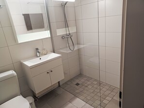 Un baño moderno con lavamanos, espejo y ducha blancos.