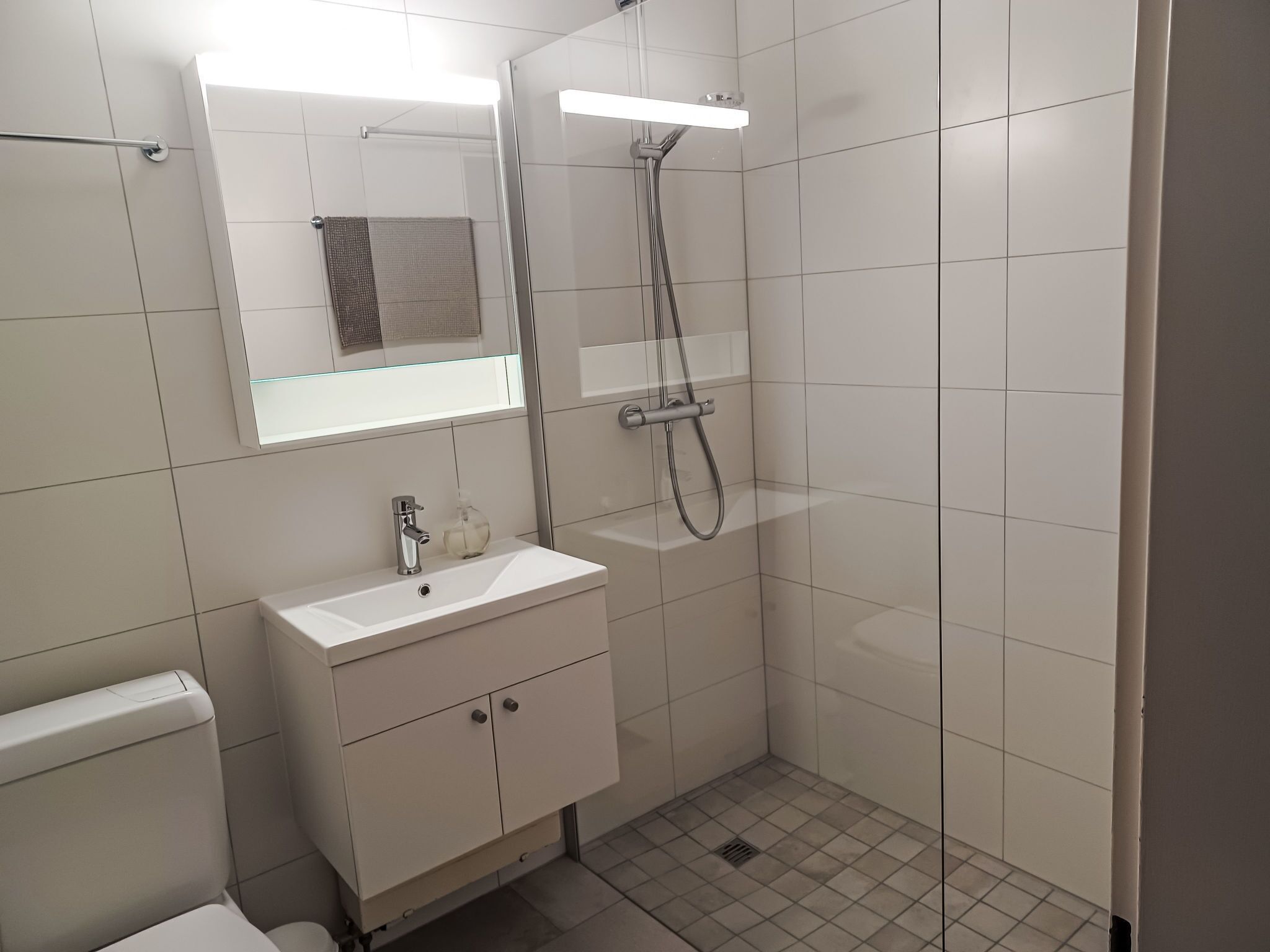 Een moderne badkamer met een wit wastafelmeubel, spiegel en douche.