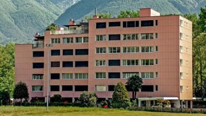 Un hôtel à plusieurs étages, doté d’un toit plat, entouré d’une végétation luxuriante et avec des montagnes en toile de fond.