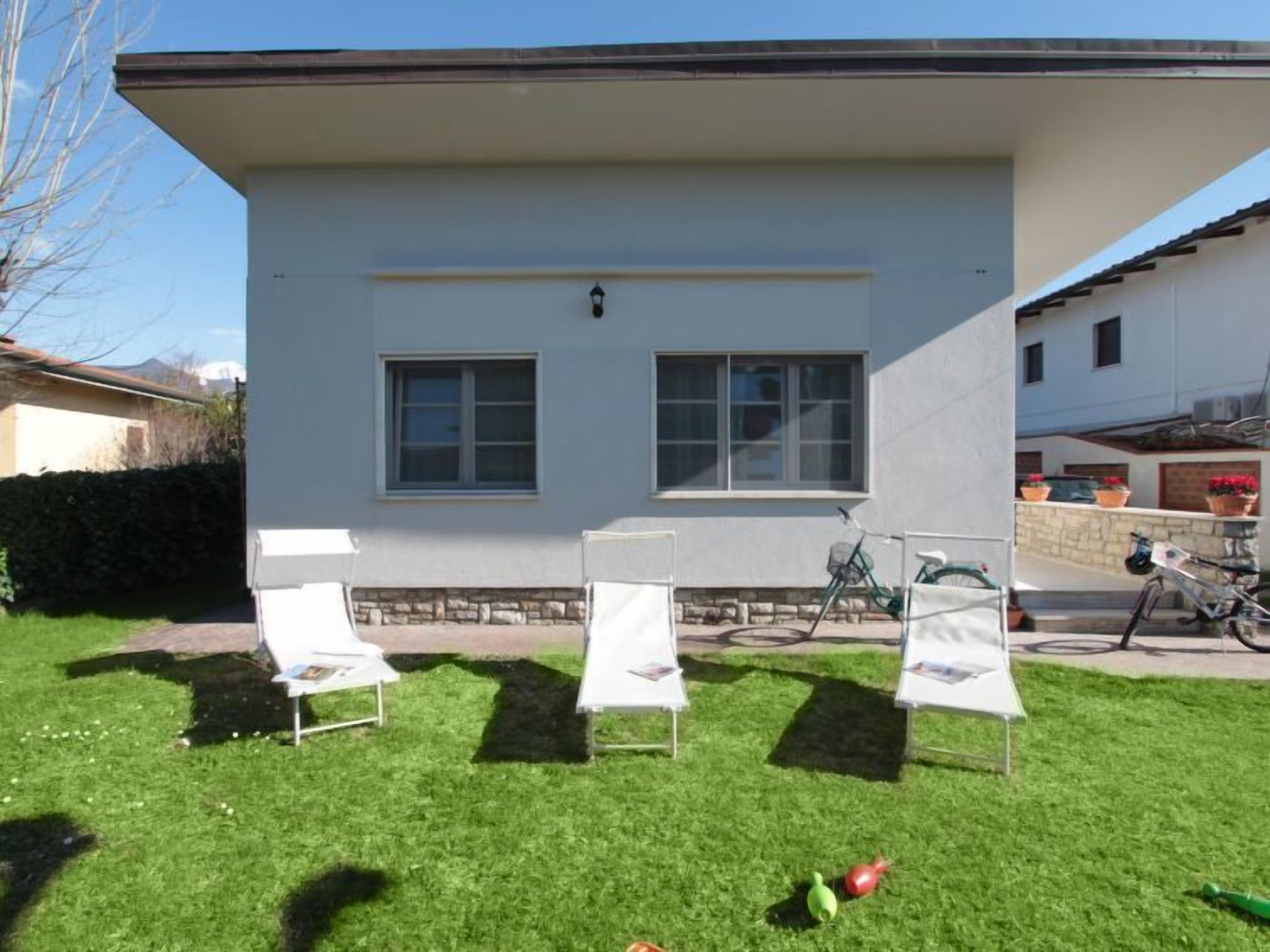 Una casa moderna de dos plantas con techo plano y fachada blanca. Hay dos ventanas en la parte frontal, y una bicicleta estacionada afuera.