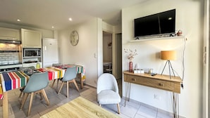 A modern kitchen with a dining area, a TV mounted on the wall, and a lamp on a wooden side table. - Les Alizés by Interhome (Carnac)