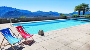 Ein Swimmingpool mit zwei Liegestühlen, einem blauen und einem roten, mit Blick auf Berge im Hintergrund.