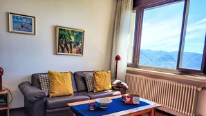 Ein Wohnzimmer mit einer Couch, einem Tisch, einem Heizkörper und einem Fenster mit Blick auf die Berge.