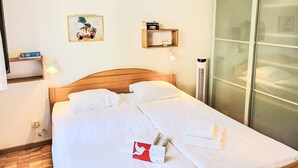 Ein ordentlich bezogenes Bett mit weißen Leinentüchern, ein Holzkopfteil, ein Nachttisch mit einer Lampe, ein gerahmtes Kunstwerk an der Wand und eine Schiebetür zur Rechten.