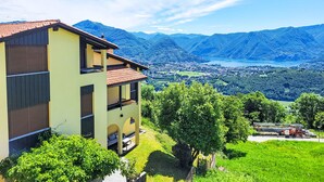 Ein mehrstöckiges Gebäude mit rotem Ziegeldach, einem Balkon und Blick auf eine gebirgige Landschaft mit einem See.
