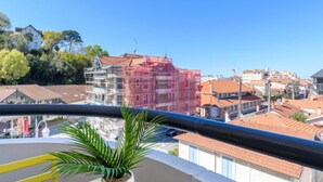 Un balcó amb una planta en test, una cadira groga i vista d'un edifici en construcció amb bastiments.