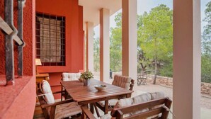 Une terrasse extérieure avec une table et des chaises en bois, entourée d’un mur rouge et de grandes fenêtres.