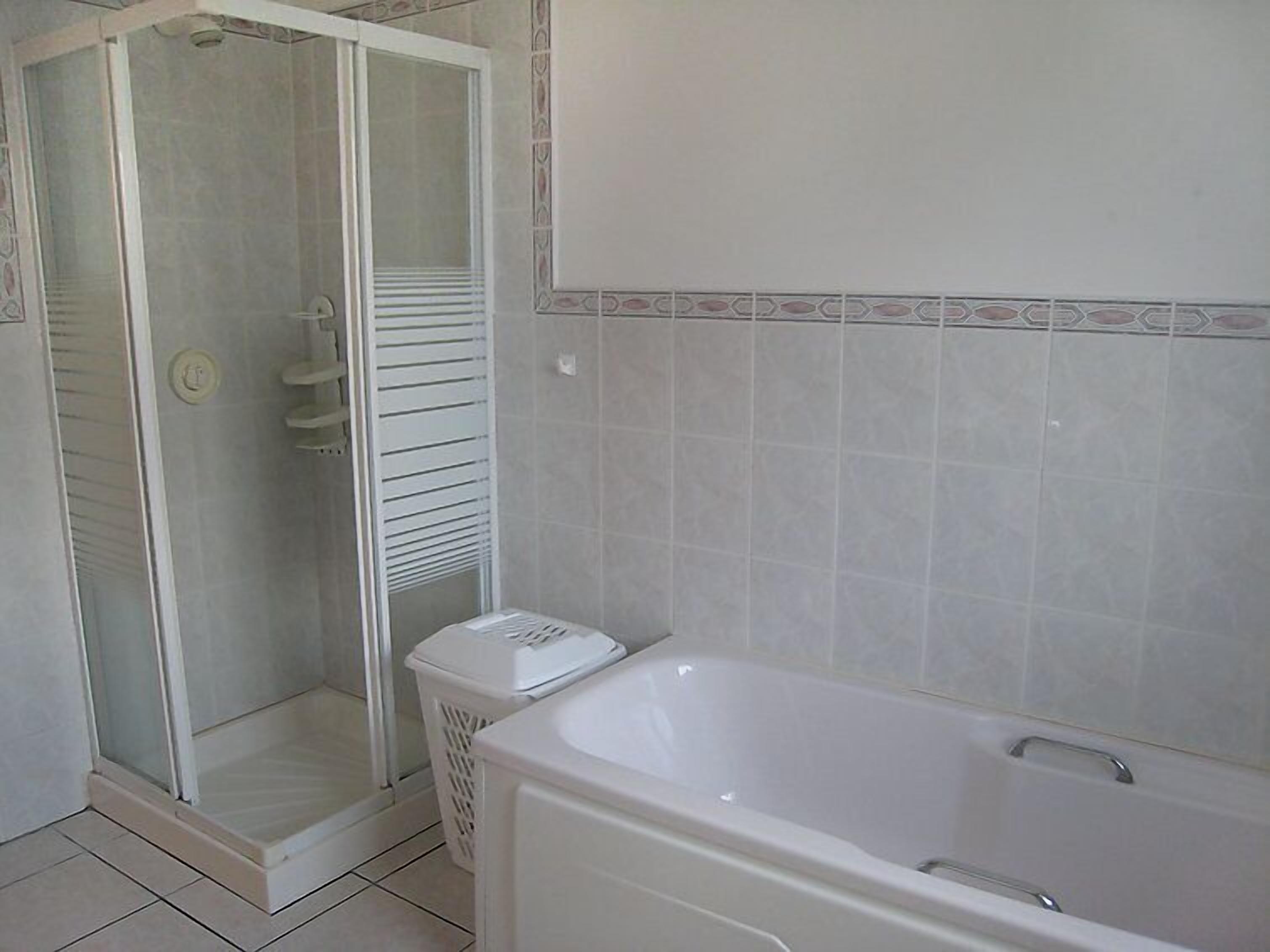 Une salle de bain avec une douche à parois de verre, une baignoire blanche et des murs carrelés.