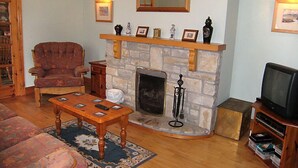 Una sala de estar con chimenea de piedra, un sillón de madera, un sofá, una mesa de centro y un televisor sobre un mueble de madera.