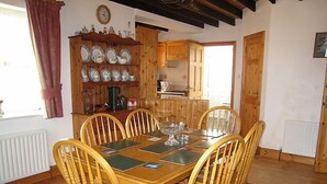 Comedor con mesa y sillas de madera, cocina al fondo y alfombra estampada en el suelo.