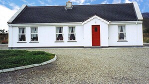 Una casa de un solo piso de color blanco, con una puerta roja, techo negro y entrada de grava.