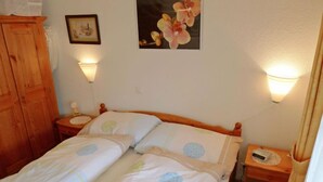 Een tweepersoonsbed met bloemenbeddengoed, twee nachtkastjes met lampen, een houten garderobe en een ingelijst schilderij aan de muur.