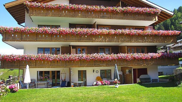 Een meerhoog gebouw met balkons versierd met bloemen, een overdekt terras en een gazon.