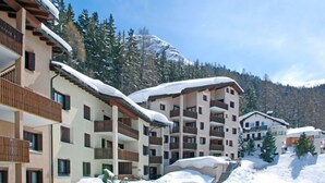 Ein mehrstöckiges Hotel mit Balkonen, schneebedeckten Dächern und einer Bergkulisse.