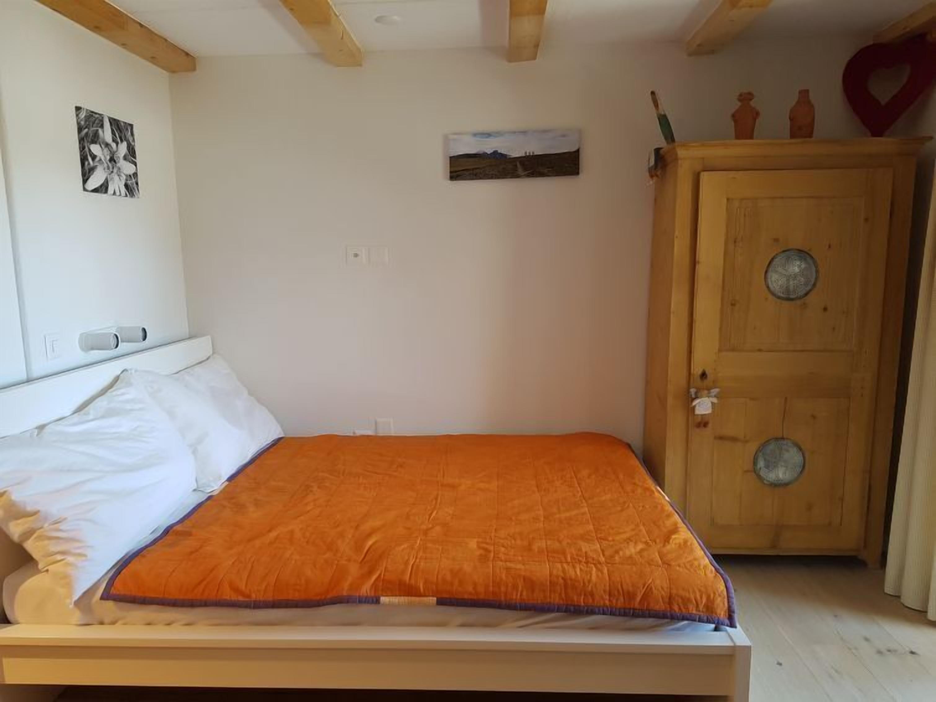 A bedroom with a bed, a wooden wardrobe, and two wall-mounted pictures.