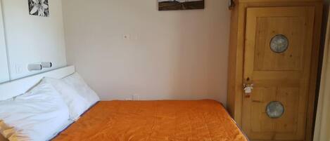 A bedroom with a bed, a wooden wardrobe, and two wall-mounted pictures.