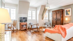 Ein gemütliches Wohnzimmer mit Holzboden, einem weißen Sofa, einem Fernseher und einer Holzkommode.