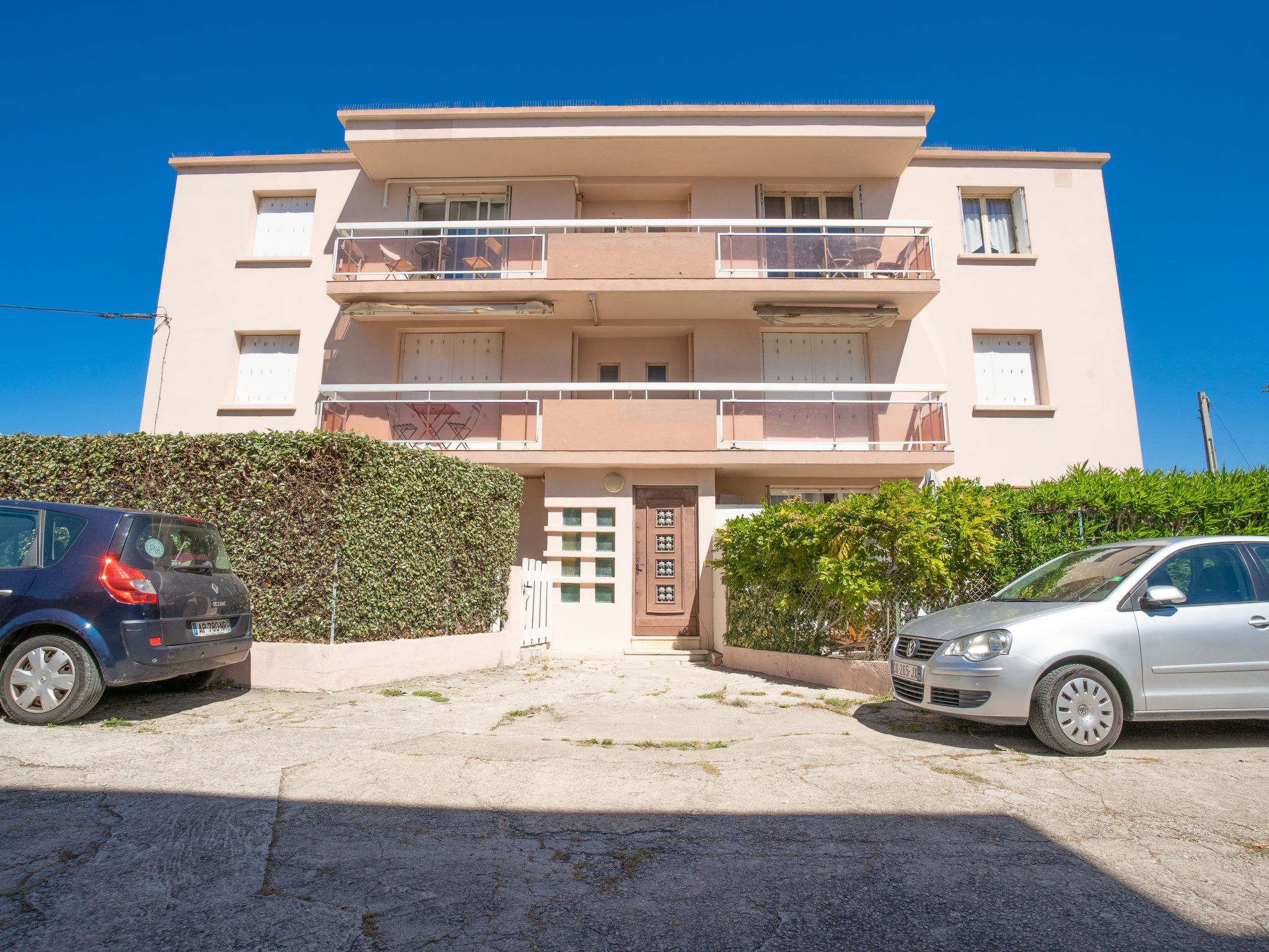 A two-story building with a flat roof, balconies, and a gated entrance.