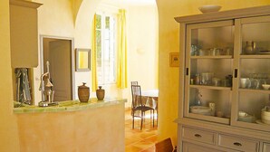 Eine Küche mit Fliesenboden, einer Spüle an einem Tresen, einem Schrank mit Gläsern und einem Essbereich mit Stühlen und einem Tisch.