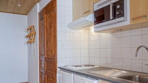 Una cocina compacta con azulejos blancos, microondas integrado, lavamanos y lavavajillas.