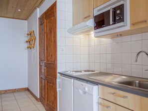 A compact kitchen with white tiles, a built-in microwave, a sink, and a dishwasher.