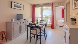 Un comedor con una mesa dispuesta para dos personas, un televisor en un mueble y una ventana con cortinas rojas.