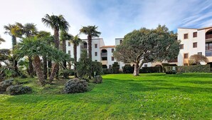 Un jardín bien cuidado con palmeras y césped frente a un edificio con balcones y ventanas arqueadas.