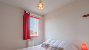 Un dormitorio con cama, mesita de noche, lámpara, ventana con cortinas y radiador.